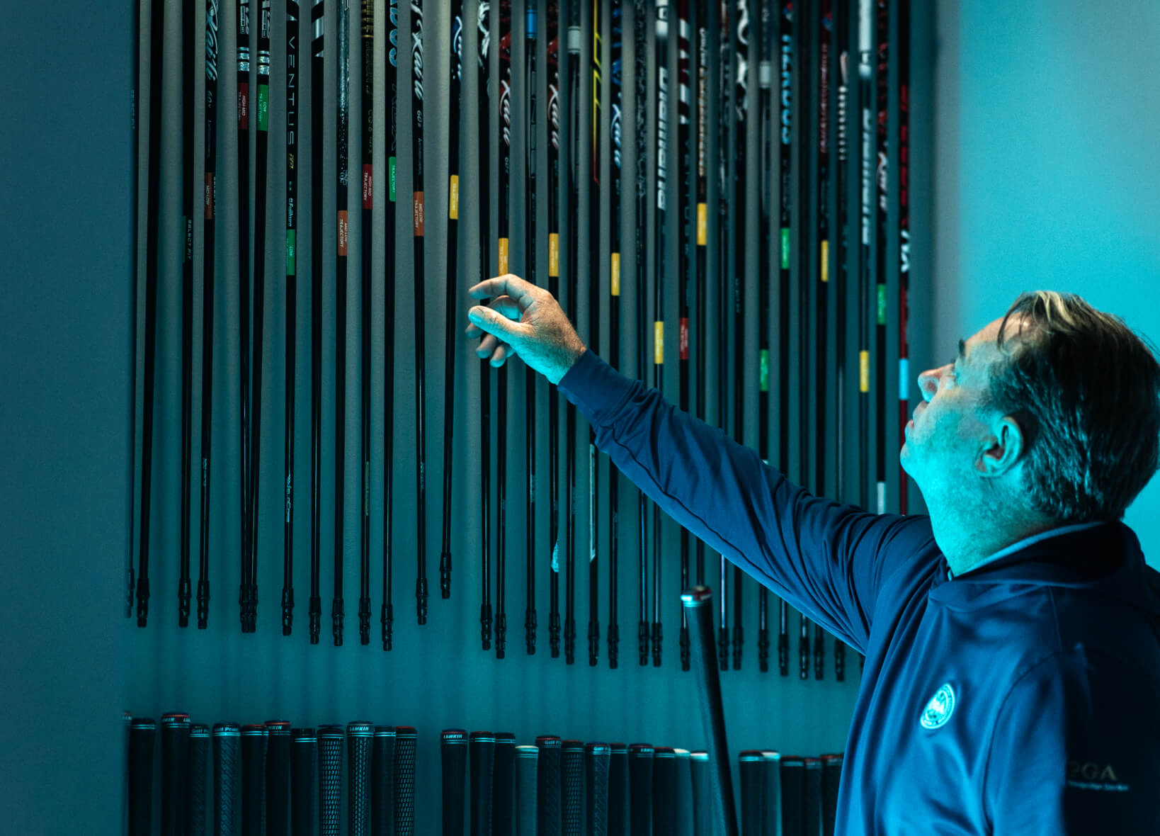 Studio Golf fitter selecting shafts from a wall of golf club options.