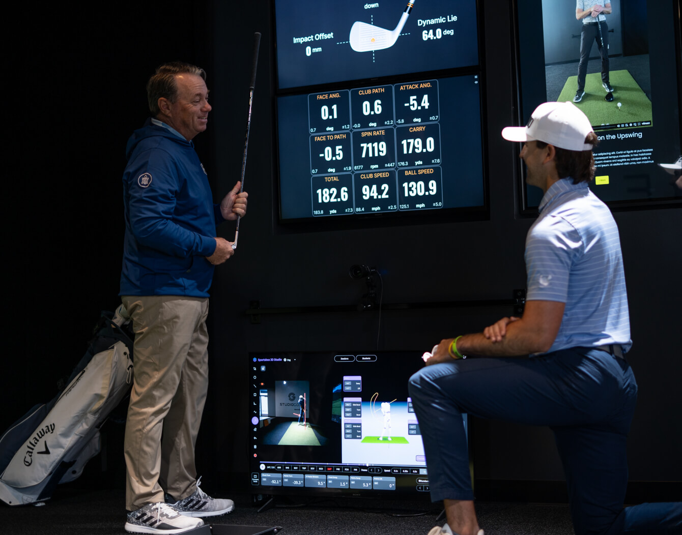Golf instructor and student reviewing swing data on TrackMan screens in a practice bay.