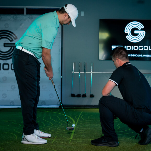 Coach working with golfer on putting technique at Studio Golf indoor training facility.