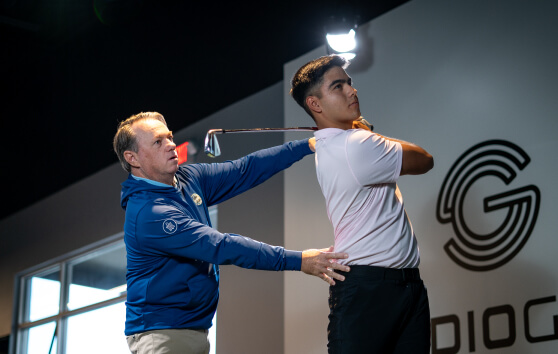 Instructor guiding golfer’s swing mechanics inside a Studio Golf bay with TrackMan technology.