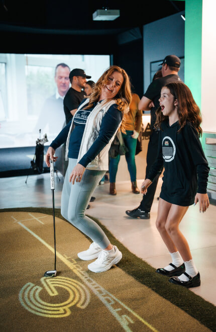 Two women laughing and putting on an indoor green at Studio Golf during an event.