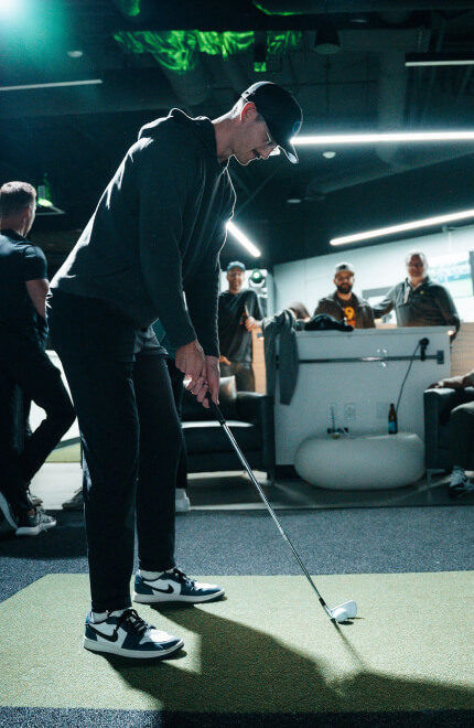 Man lining up a putt in a high-tech golf bay at Studio Golf while guests watch.
