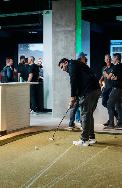 Golfer taking a putt on the indoor green while a group of guests watches at Studio Golf.