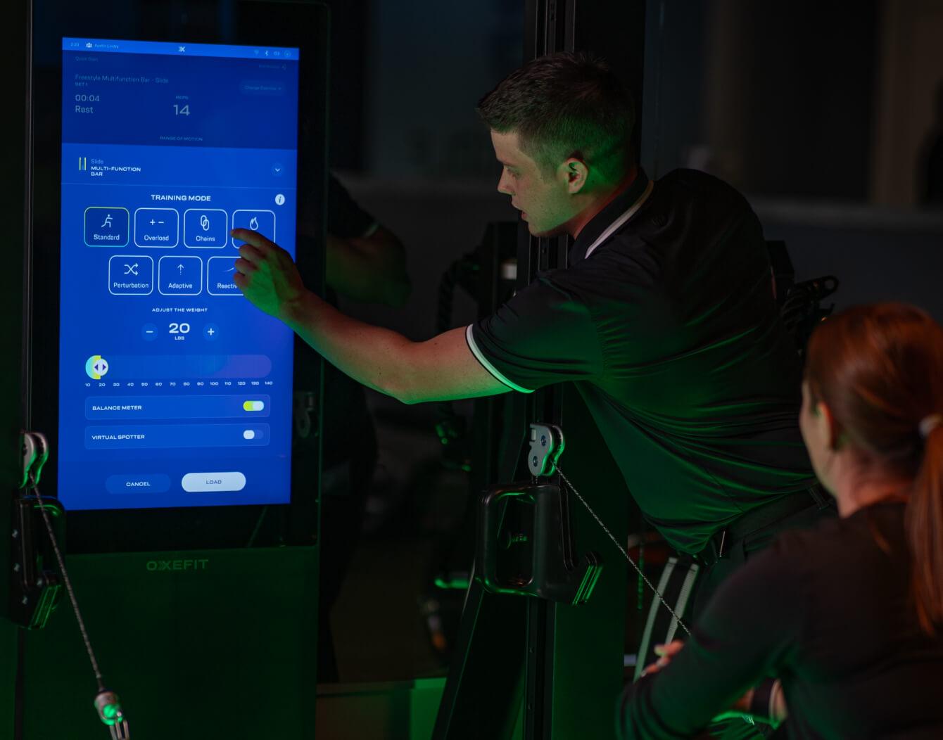 Close-up of OxeFit Smart Gym digital interface with a trainer assisting a member.